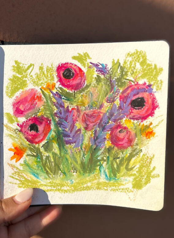 hand holding sketchbook to show a pastel painting of a meadow with semi abstract wild flowers on green background