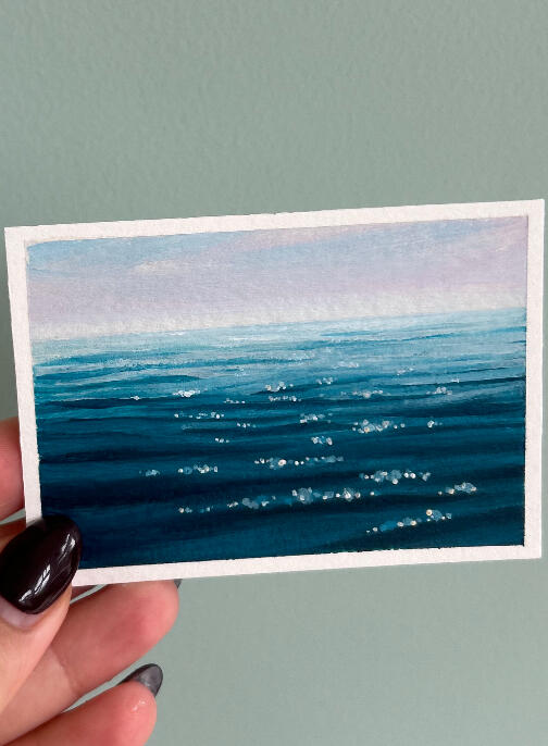 sold seascape aceo painting on paper, showing a blue ocean surface view and hazy horizon. painting is showed held by hand