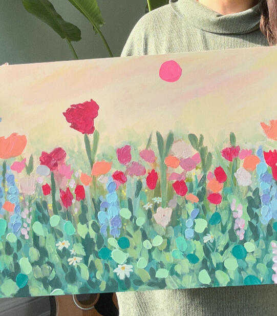 floral textured painting of a meadow in green, blue, pink, lilac and orange tones, in a semi abstract / modern impressionistic style. Pink sun in the sky. and a muted yellow background. painting is held by artist which is only partially visible in picture