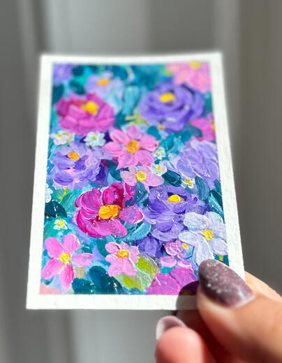 hand holding aceo sized floral painting in hues of pink lilac blue and green